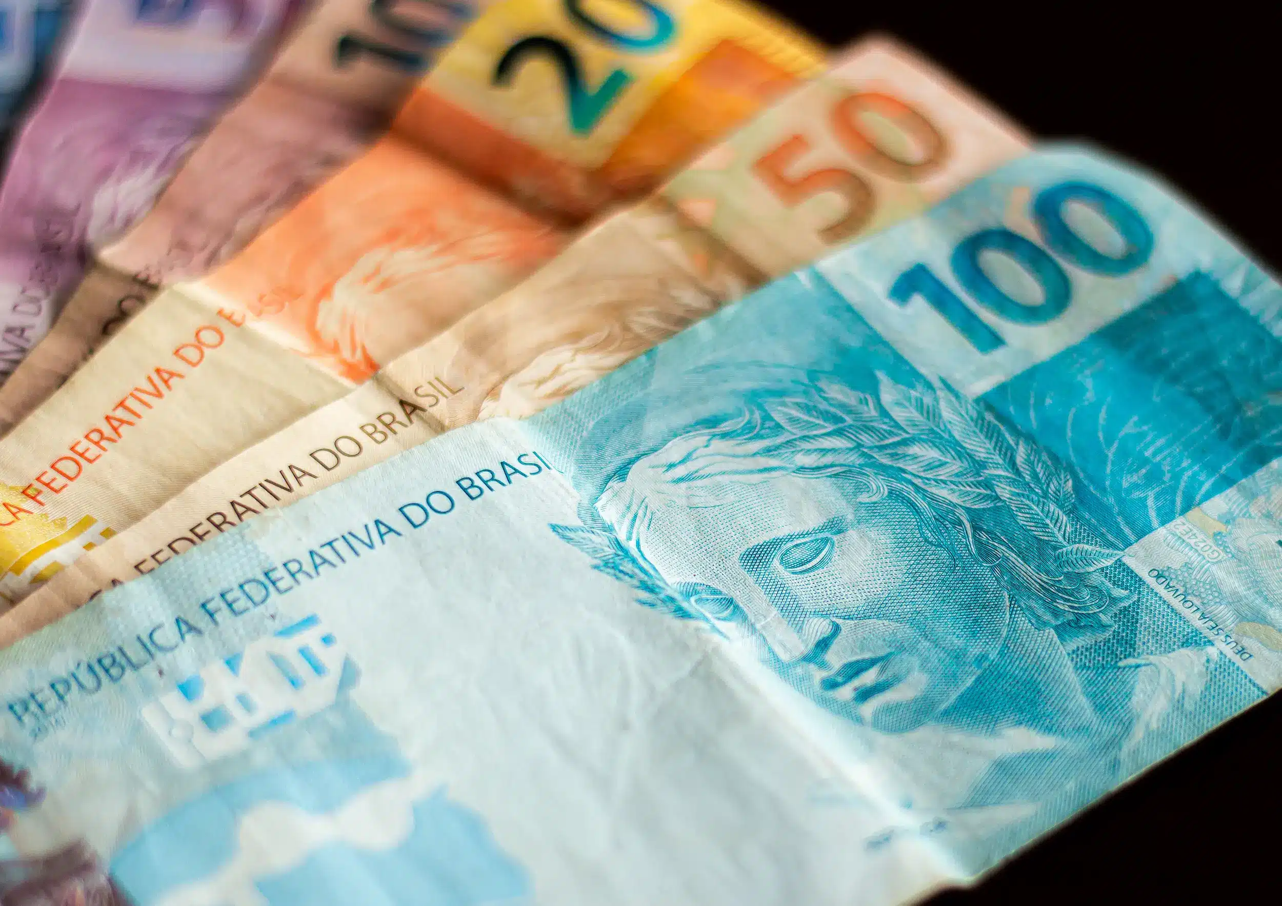 Notas de dinheiro com destaque para a cédula de 100 reais, representando os pagamentos do INSS para finais 4, 5, 6 e 7.