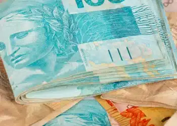 Notas de dinheiro coloridas com destaque para a cédula de 100 reais em azul, representando o tema de pagamentos de março do INSS.