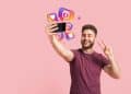 Homem tirando selfie com smartphone enquanto ícones de redes sociais representam novos recursos premium do Instagram como visualização anônima de stories.