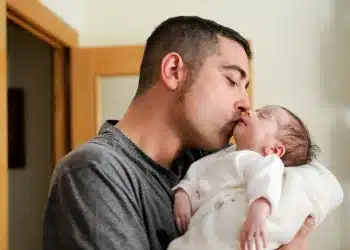 Pai segurando e beijando um recém-nascido, representando o fortalecimento do vínculo familiar após aprovação do Senado para ampliar gradualmente a licença paternidade no Brasil.