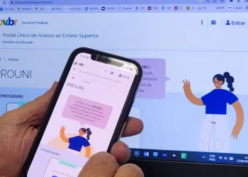 Pessoa acessando o site do Prouni no celular e na tela do computador, com informações sobre a lista de espera.