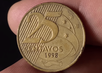 Close-up do anverso de uma moeda de 25 centavos de 1998, mostrando os detalhes da data e da bandeira estilizada em fundo escuro.