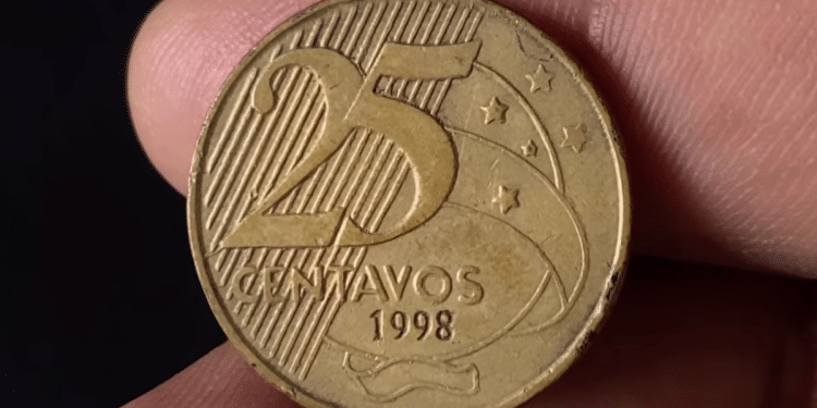 Close-up do anverso de uma moeda de 25 centavos de 1998, mostrando os detalhes da data e da bandeira estilizada em fundo escuro.