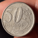Close nítido de uma moeda de 50 centavos do Brasil, ano 2000, destacando o numeral 50 e as estrelas do Cruzeiro do Sul, segurada entre os dedos para inspeção de raridade.