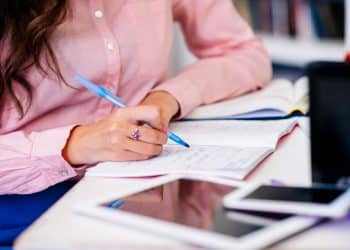 Preparação para o Enem 2026: estudante anotando em caderno com caneta azul e materiais de estudo sobre a mesa