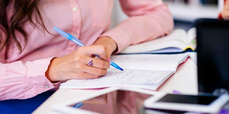 Preparação para o Enem 2026: estudante anotando em caderno com caneta azul e materiais de estudo sobre a mesa