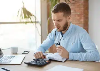 Homem analisando contas e fazendo cálculos financeiros no notebook para negociar dívidas bancárias no mutirão de renegociação