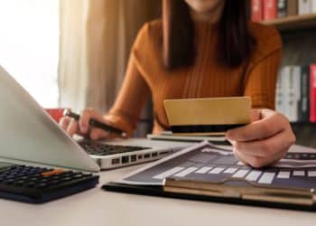 Pessoa utilizando cartão de crédito e notebook para organizar finanças e negociar dívidas bancárias.