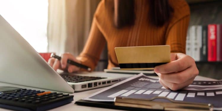 Pessoa utilizando cartão de crédito e notebook para organizar finanças e negociar dívidas bancárias.