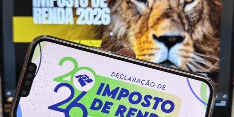 Celular com app da declaração do Imposto de Renda 2026 e leão da Receita Federal ao fundo