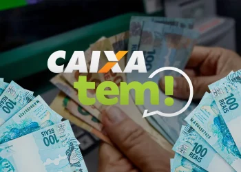 Mãos contando notas de R$ 100 em frente a um caixa eletrônico com a logo do Caixa Tem em destaque, representando a necessidade de desbloqueio do aplicativo para acessar o pagamento do Pé-de-Meia depositado pelo MEC em março de 2026