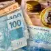 Notas e moedas do real brasileiro, incluindo cédulas de R$100 e R$50 e uma moeda de R$1, representando o contexto de pagamentos do INSS em 2026.