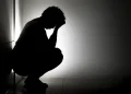 Silhueta de pessoa agachada com a cabeça entre as mãos em ambiente escuro, representando sofrimento emocional causado pelo pensamento acelerado