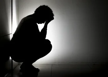 Silhueta de pessoa agachada com a cabeça entre as mãos em ambiente escuro, representando sofrimento emocional causado pelo pensamento acelerado
