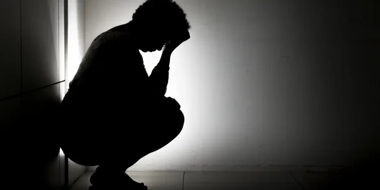 Silhueta de pessoa agachada com a cabeça entre as mãos em ambiente escuro, representando sofrimento emocional causado pelo pensamento acelerado