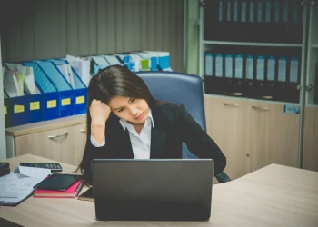 Profissional com aparência desanimada trabalhando no notebook em um escritório, representando frustração com a carreira.