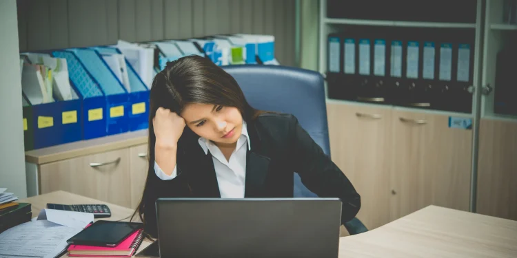 Profissional com aparência desanimada trabalhando no notebook em um escritório, representando frustração com a carreira.