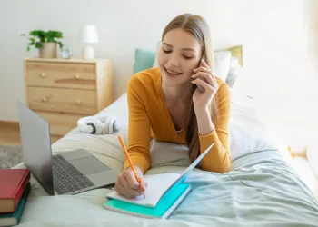 Pessoa organizando tarefas do dia em um caderno enquanto usa notebook e celular para otimizar a rotina.