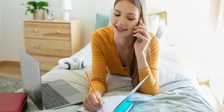 Pessoa organizando tarefas do dia em um caderno enquanto usa notebook e celular para otimizar a rotina.
