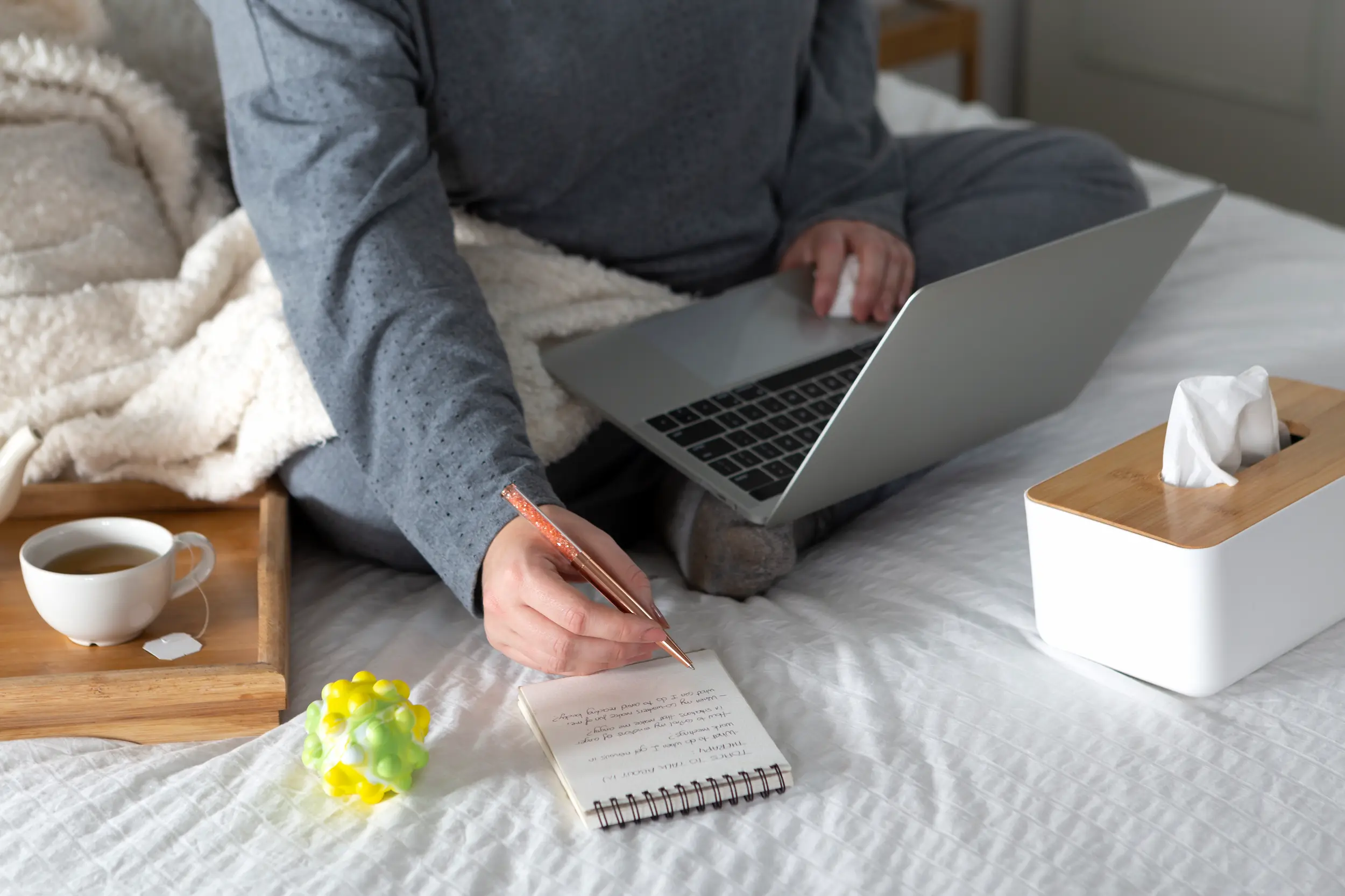 Pessoa anotando lista de tarefas enquanto utiliza notebook para planejar atividades diárias.