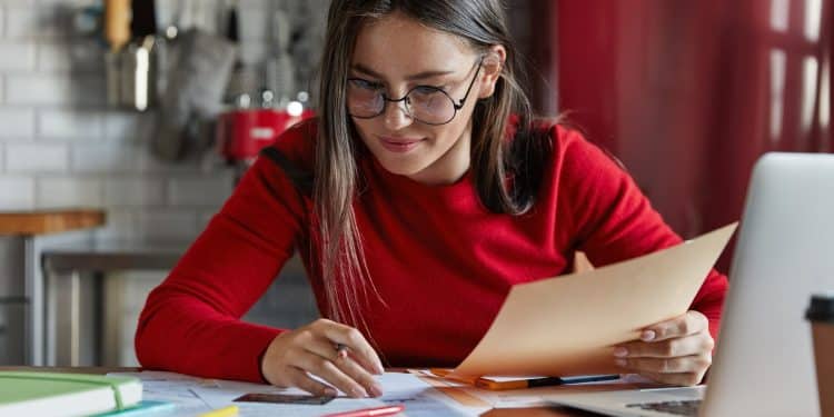 Jovem estudante com óculos revisando anotações e materiais sobre a mesa em preparação para o vestibular 2026.