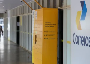 Fachada de unidade dos Correios com logomarca e locker amarelo para retirada de encomendas, representando o processo seletivo do programa jovem aprendiz Correios 2026, com 548 vagas e inscrições gratuitas.