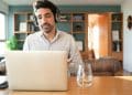 Profissional em escritório doméstico participando de reunião online pelo notebook enquanto trabalha remotamente.
