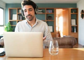 Profissional em escritório doméstico participando de reunião online pelo notebook enquanto trabalha remotamente.