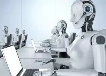 Robôs humanoides com fones de ouvido trabalhando em notebooks em ambiente de escritório, ilustrando o debate sobre automação, inteligência artificial e o futuro das profissões no mercado de trabalho.