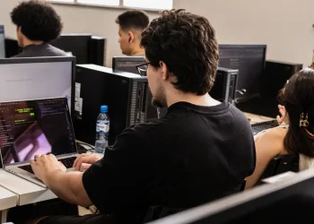 Jovens estudantes em laboratório de informática com notebooks e computadores realizando atividades práticas de cibersegurança no programa Hackers do Bem, iniciativa gratuita da Rede Nacional de Ensino e Pesquisa com mais de 25 mil vagas abertas.