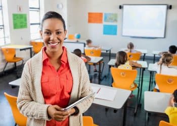Professora entrega atividade a alunos em sala de aula enquanto projeto de lei debate adicionais de insalubridade para docentes.