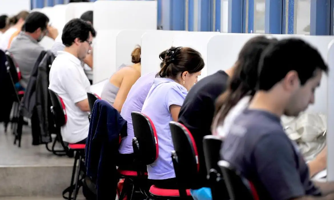 Jovens estudantes concentrados trabalhando em baias individuais, representando estagiários em ambiente de trabalho e o debate sobre remuneração obrigatória e cotas no estágio profissional