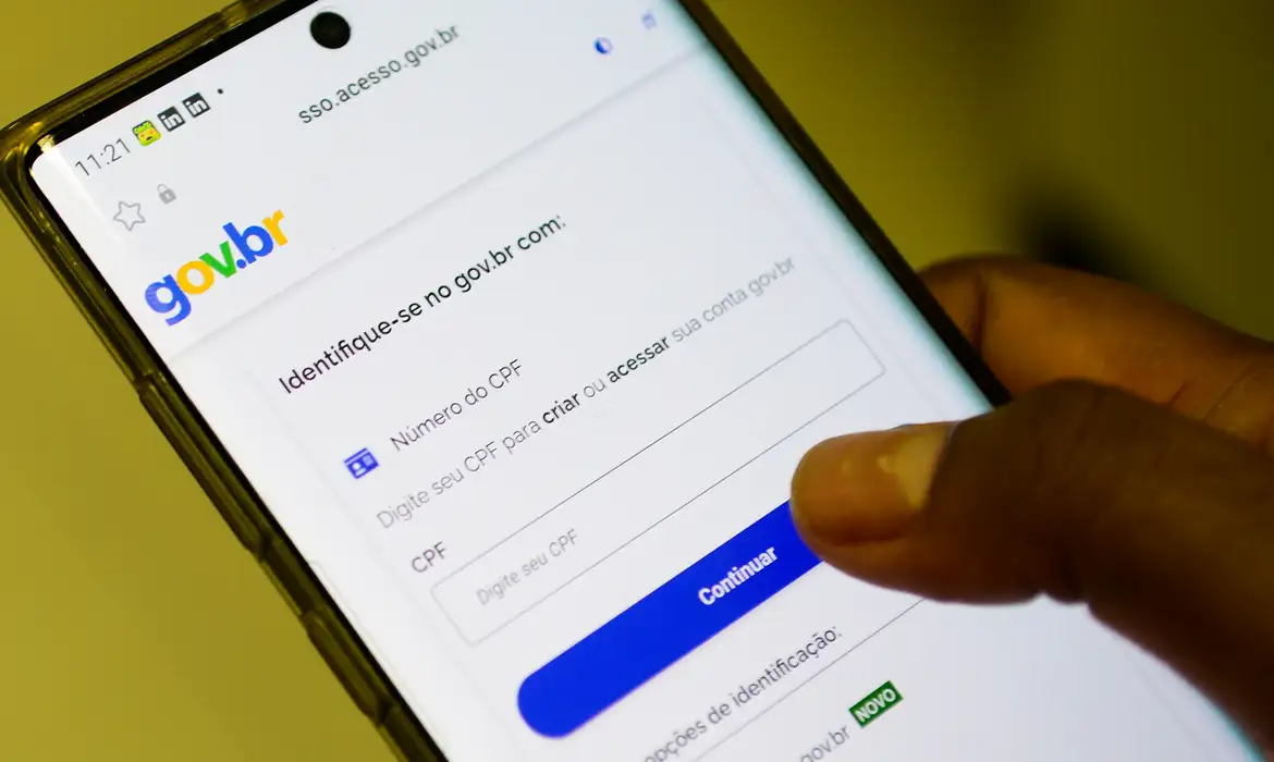 Mão segurando smartphone com a tela de login do portal gov.br aberta, mostrando o campo de CPF para identificação, representando o reforço nas regras de acesso ao aplicativo SouGov.br
