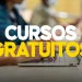 Mãos digitando em um notebook em ambiente de estudo com outras pessoas ao fundo desfocadas e a inscrição "Cursos Gratuitos" em letras brancas e amarelas em destaque, representando o acesso à plataforma QualificaPro lançada pelo governo federal para capacitar trabalhadores