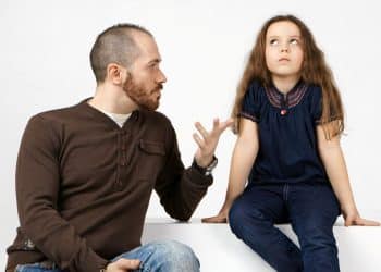 Um homem adulto com expressão de cobrança gesticula enquanto fala com uma menina; a criança desvia o olhar com semblante de cansaço e frustração, representando a imaturidade emocional parental.