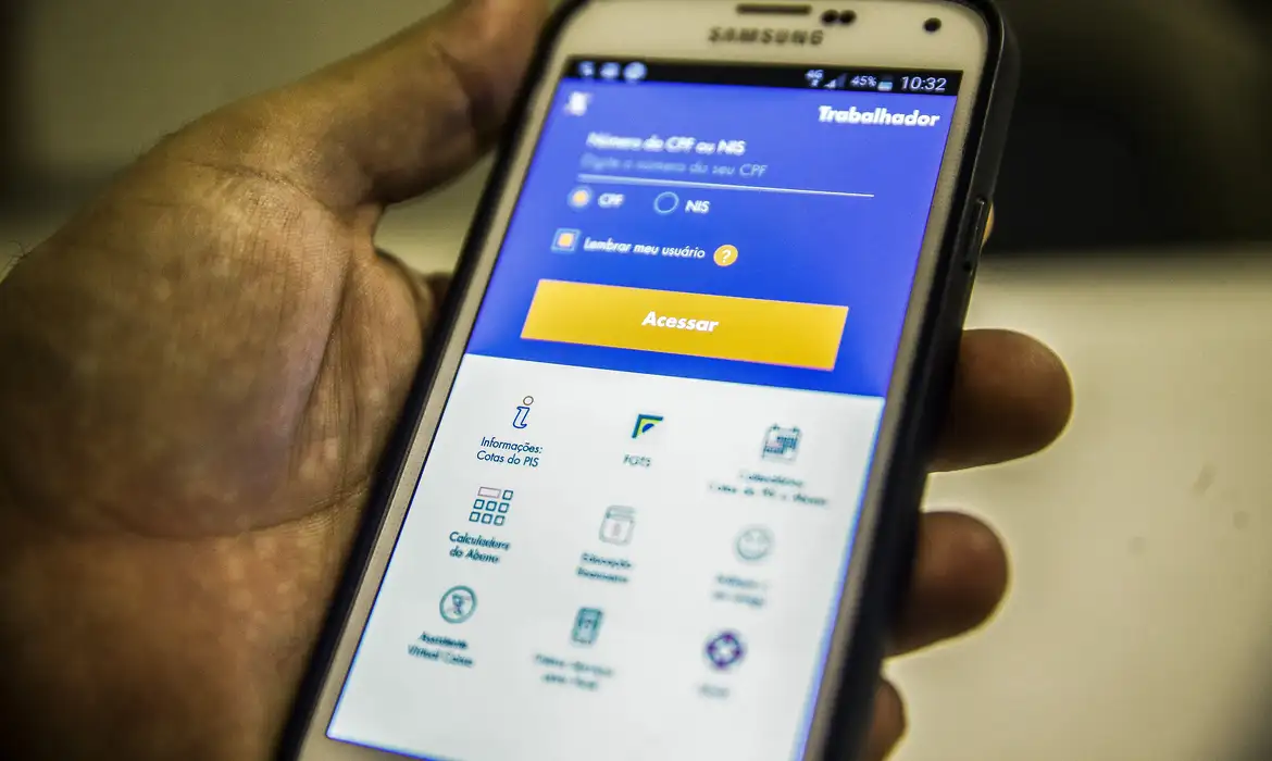 Mão segurando smartphone Samsung com aplicativo do Trabalhador aberto na tela de login, exibindo campo para CPF ou NIS e botão de acesso ao FGTS para solicitação do saque