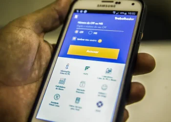 Mão segurando smartphone Samsung com o aplicativo do FGTS aberto na tela de login, exibindo campos para inserção de CPF ou NIS, ilustrando como solicitar o Saque Calamidade do FGTS de forma digital