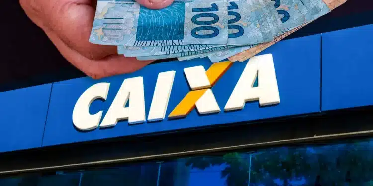 Mão segurando notas de cem reais na frente da fachada azul de uma agência da Caixa Econômica Federal