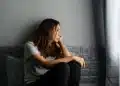 Mulher sentada sozinha olhando pela janela com expressão pensativa representando sinais de sofrimento emocional e alerta para a saúde mental.
