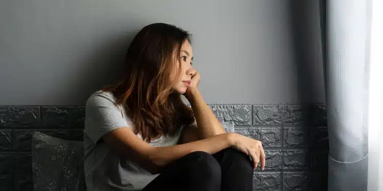 Mulher sentada sozinha olhando pela janela com expressão pensativa representando sinais de sofrimento emocional e alerta para a saúde mental.