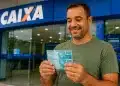 Trabalhador segura notas de real em frente à Caixa Econômica Federal, representando a solicitação do saque de até R$ 6.220 do FGTS.
