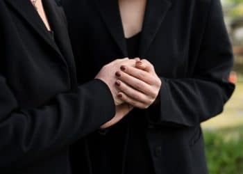 Duas pessoas vestidas de preto segurando as mãos em momento de luto e apoio emocional.