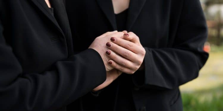 Duas pessoas vestidas de preto segurando as mãos em momento de luto e apoio emocional.