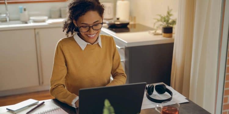 Mulher trabalhando remotamente em home office, utilizando notebook e organizando seu espaço de trabalho em casa.