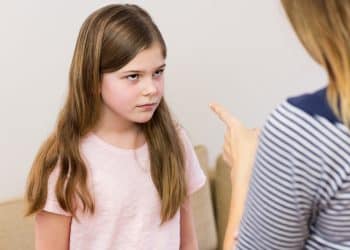 Adulto apontando o dedo indicador para criança de expressão séria e resistente em ambiente doméstico