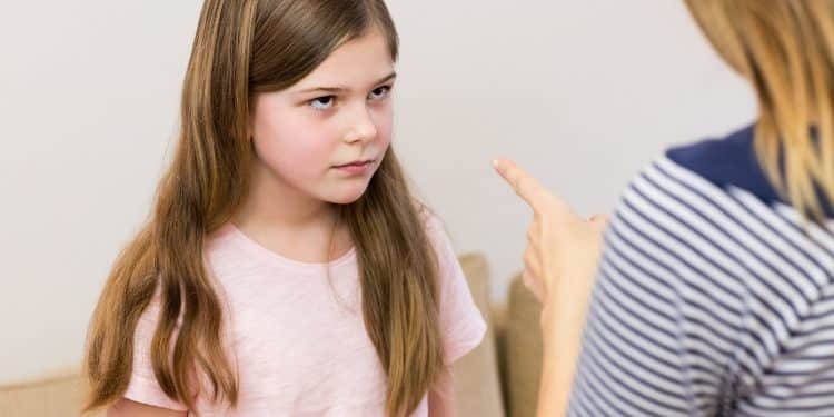 Adulto apontando o dedo indicador para criança de expressão séria e resistente em ambiente doméstico