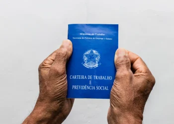 Duas mãos seguram uma carteira de trabalho azul em fundo claro