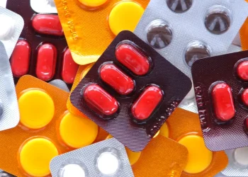 Diversas cartelas de medicamentos coloridas — vermelhas, amarelas e cinzas — espalhadas, ilustrando a nova lei brasileira que permite a instalação de farmácias e drogarias dentro de supermercados