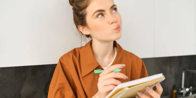 Pessoa escrevendo em um caderno enquanto estuda regras da língua portuguesa.