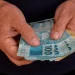 Aposentado segurando notas de real referente ao pagamento da segunda parcela do 13º do INSS.